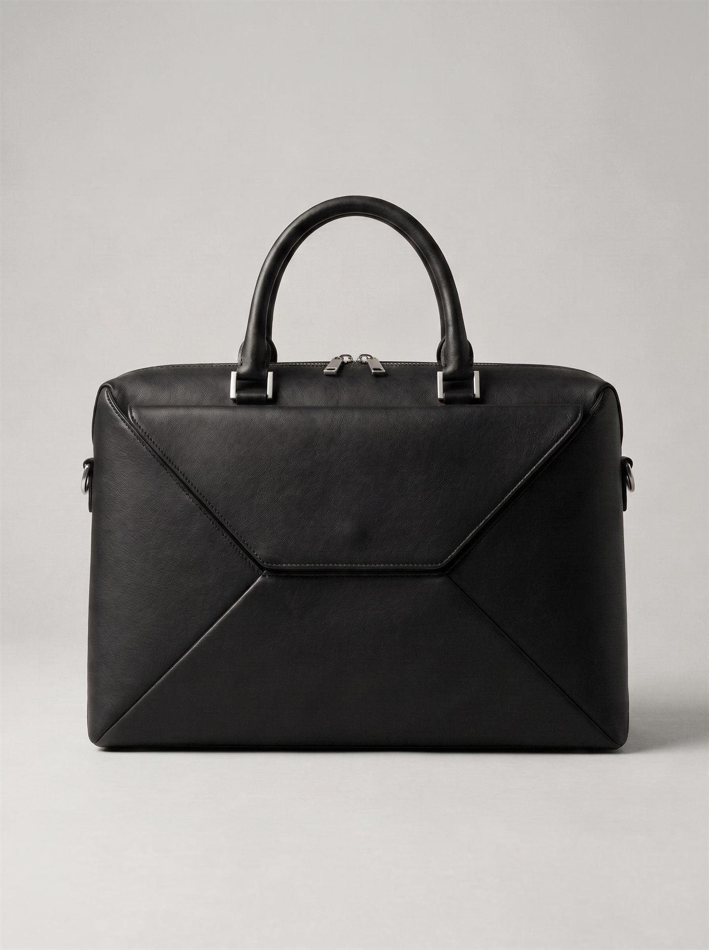 The briefcase photographed square on, 420 by 310 millimetres: a black full-grain leather front panel creased into four facets around a central envelope flap, twin rolled handles, twin zip sliders at the top edge.