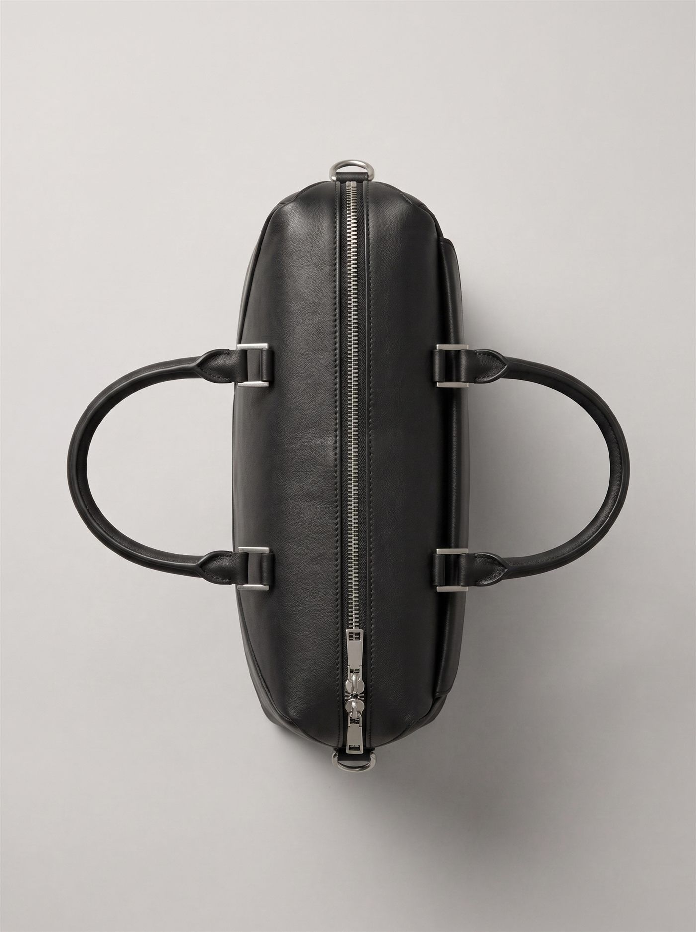 The briefcase from directly above, closed: the metal zip track running the length of the top edge with two sliders parked centre, the rolled handles held by brushed steel keepers.