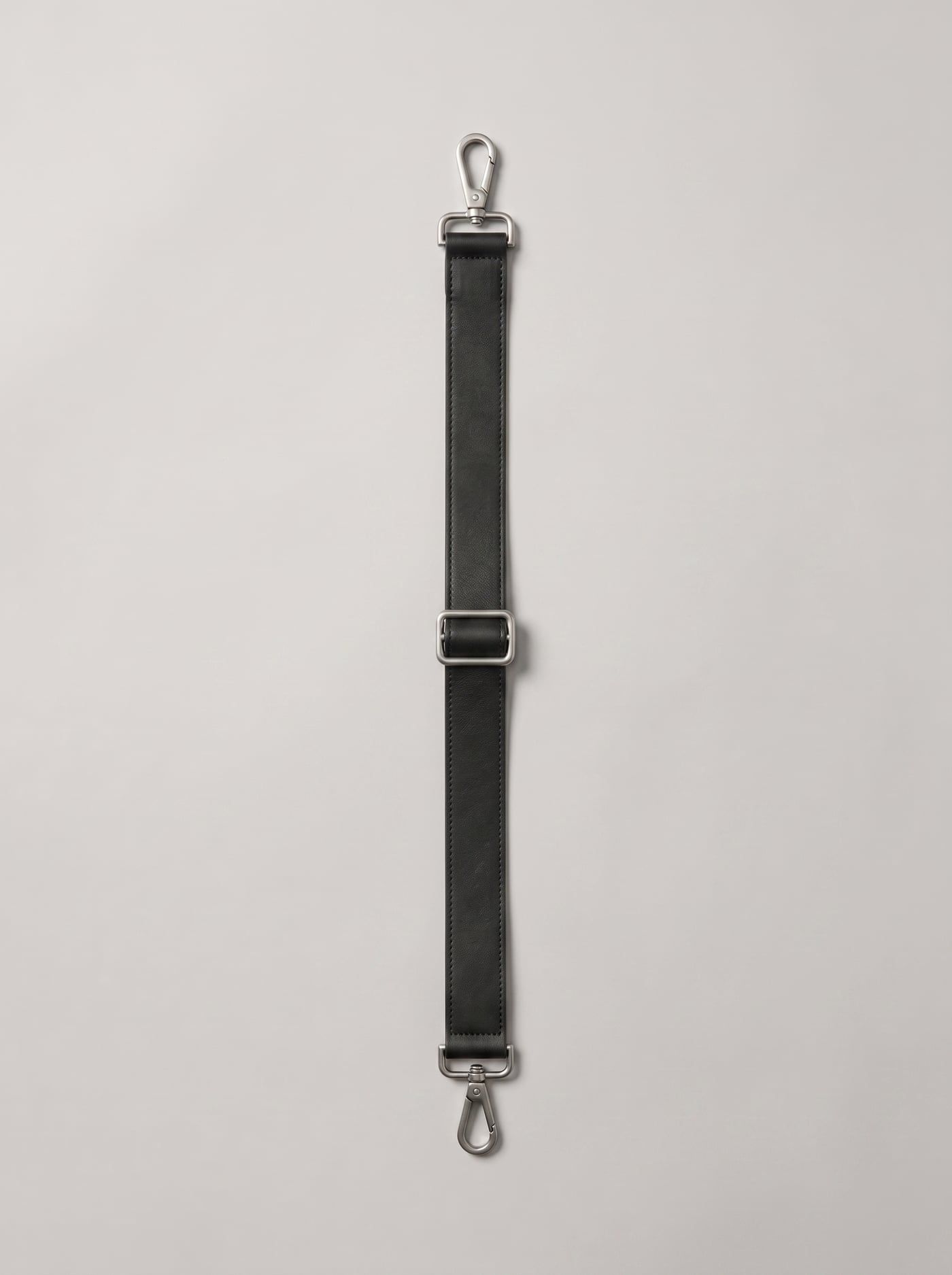 The detachable shoulder strap laid flat: leather with a centre slide adjuster and a brushed steel swivel clip at each end.
